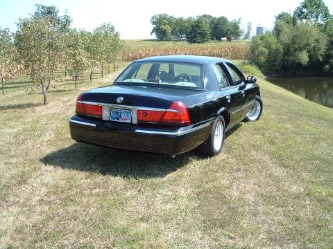 2001 Mercury Grand Marquis - The rear passenger side of a black 2001 Mercury Grand Marquis is shown parked on a grassy incline next to a pond. The car has an Indiana li…