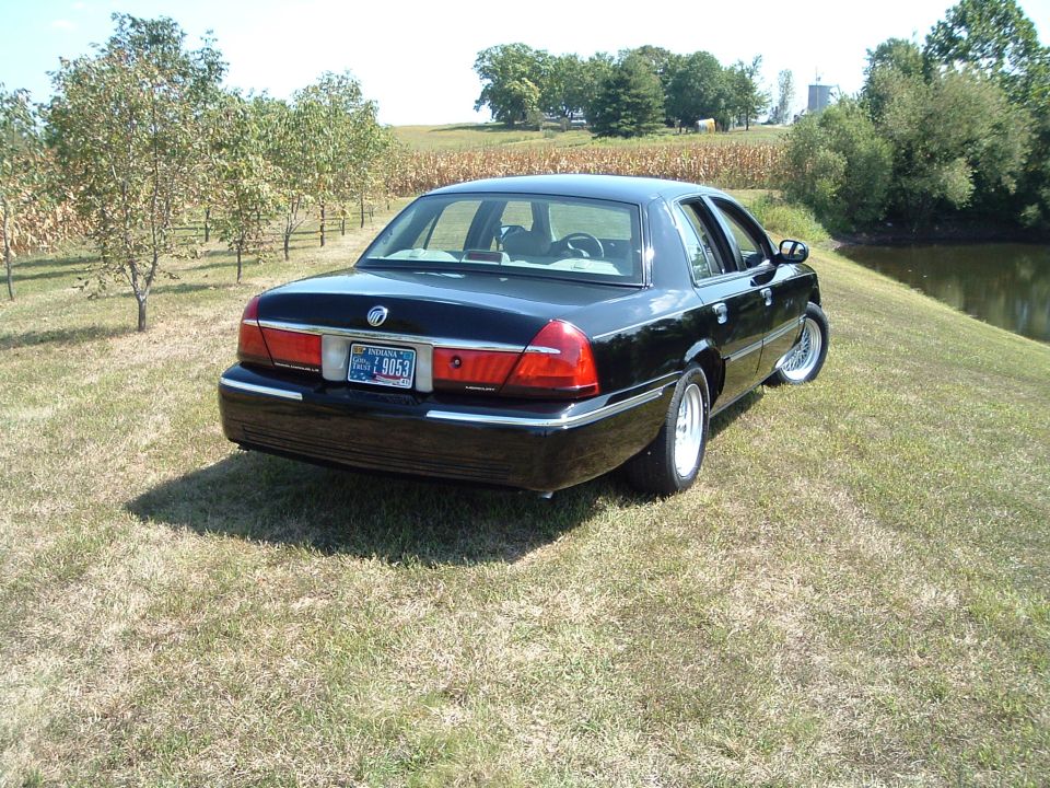 Black 2001 Mercury Grand Marquis, rear passenger side view, parked on grass by a pond.