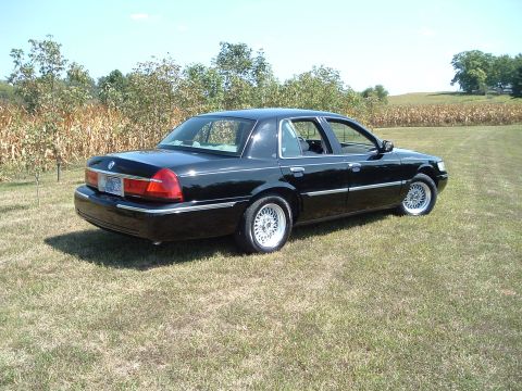 2001 Mercury Grand Marquis - A black 2001 Mercury Grand Marquis is parked on a grassy field with a cornfield in the background. The sedan is viewed from the rear quarte…