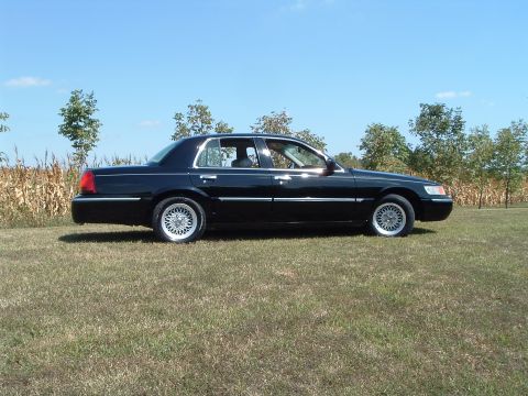 2001 Mercury Grand Marquis - A black 2001 Mercury Grand Marquis is parked on a grassy field with trees and a cornfield in the background under a clear blue sky.