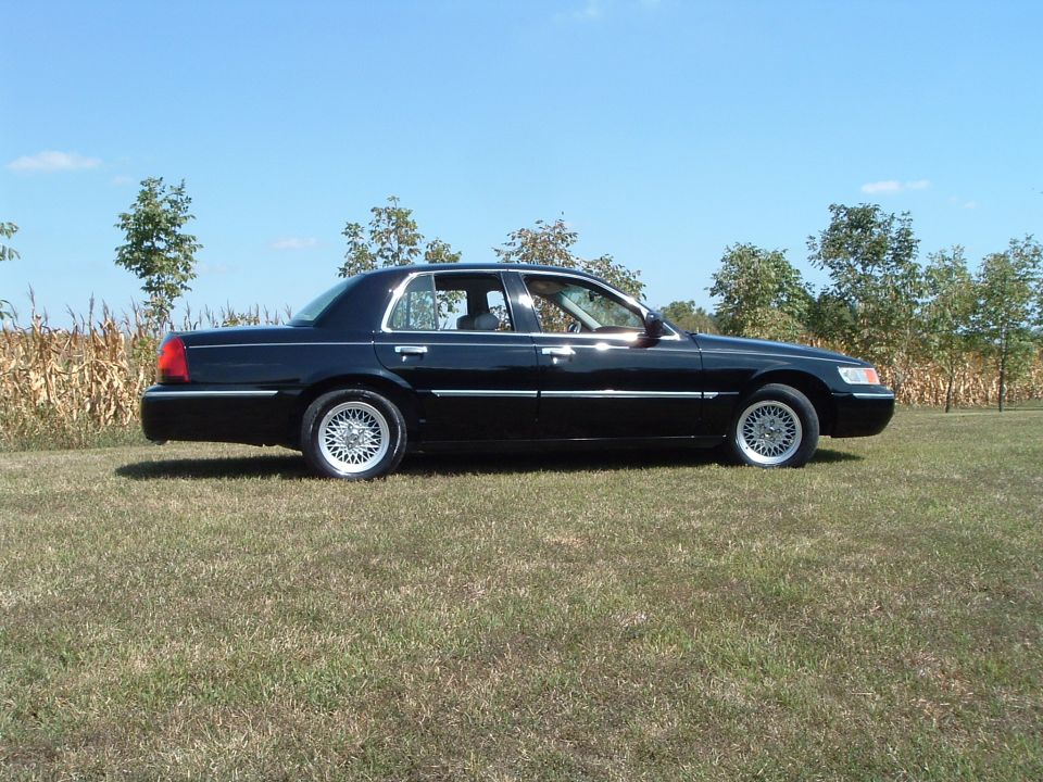 Black 2001 Mercury Grand Marquis parked on grass with trees and cornfield.