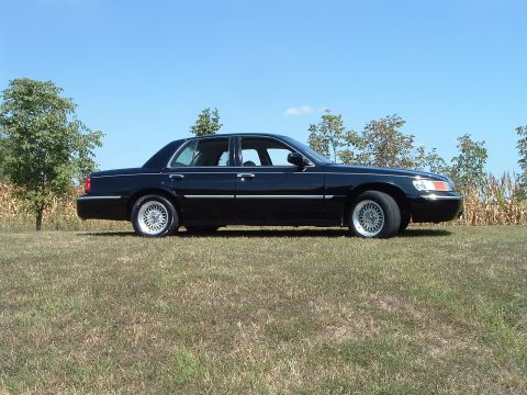 2001 Mercury Grand Marquis - A black four-door sedan is parked on a grassy hill with trees and a cornfield in the background under a clear blue sky.