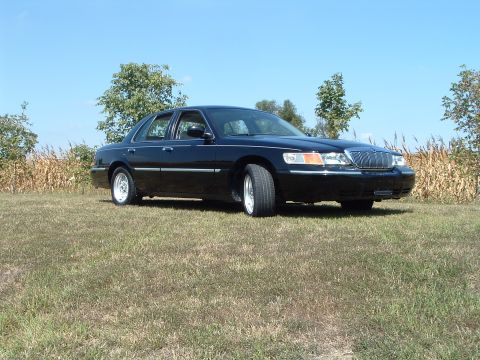 2001 Mercury Grand Marquis - A black 2001 Mercury Grand Marquis sedan is parked on a grassy field with a cornfield and trees in the background under a clear blue sky.