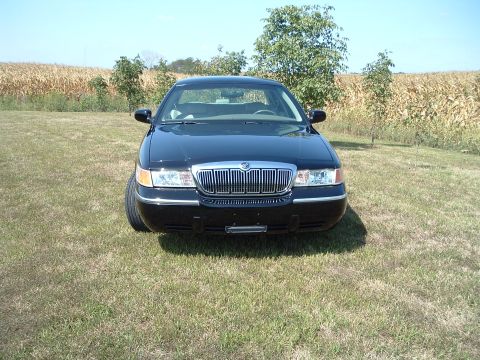 2001 Mercury Grand Marquis - The front view of a black Mercury Grand Marquis is parked on a grassy field with a cornfield in the background. The car has chrome trim aro…