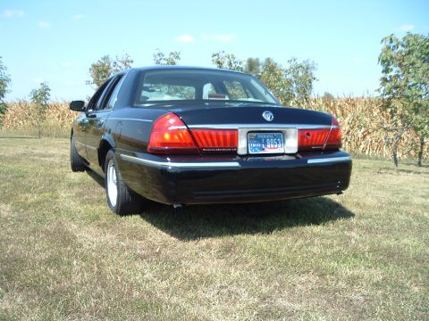 2001 Mercury Grand Marquis - The rear passenger side of a black 2001 Mercury Grand Marquis is shown parked on a grassy field with a cornfield and trees in the backgroun…