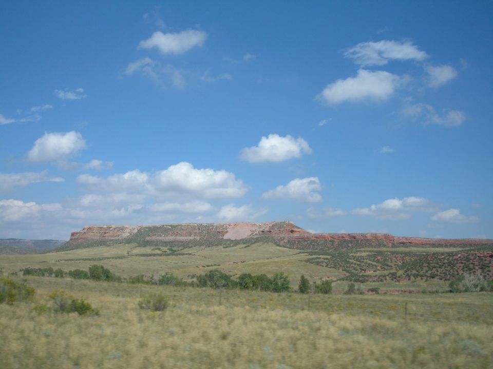 Dry grassland with rolling hills and a mesa under a blue sky with clouds.