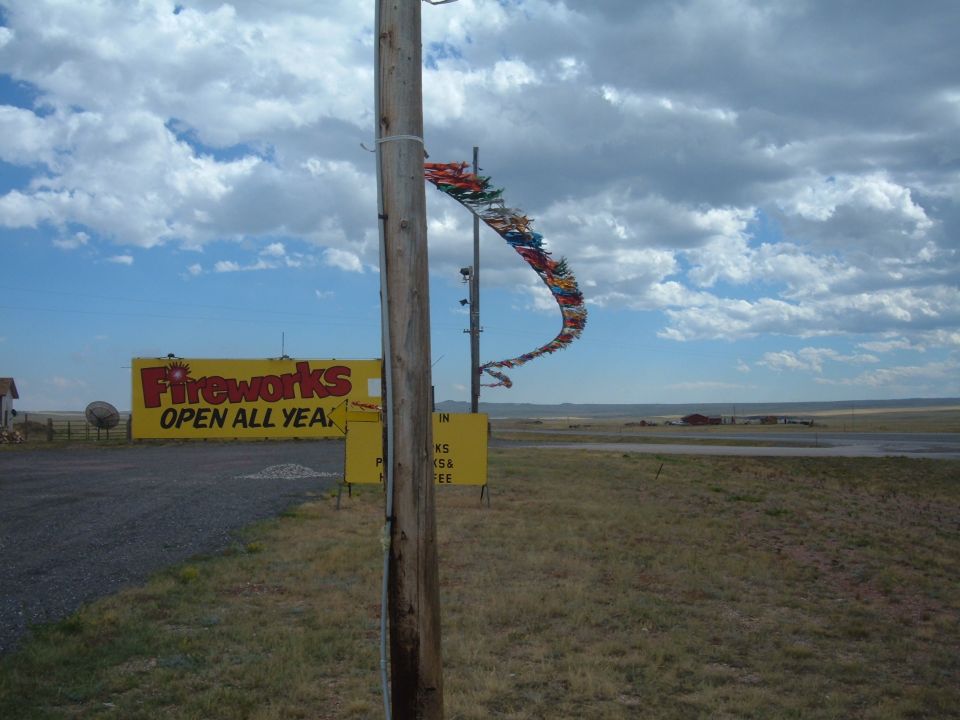 Fireworks sign next to a wooden pole with streamers, in a rural landscape.
