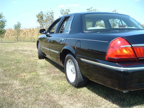 2001 Mercury Grand Marquis - The rear passenger side of a black 2001 Mercury Grand Marquis is shown parked on a grassy field with a cornfield and trees in the backgroun…