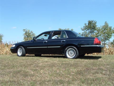 2001 Mercury Grand Marquis - A black 2001 Mercury Grand Marquis sedan is parked on a grassy field with corn stalks and trees in the background under a clear blue sky.