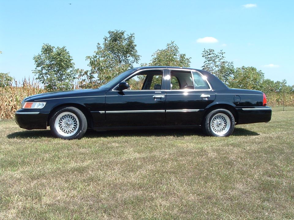 Black 2001 Mercury Grand Marquis sedan parked on grass, side view.