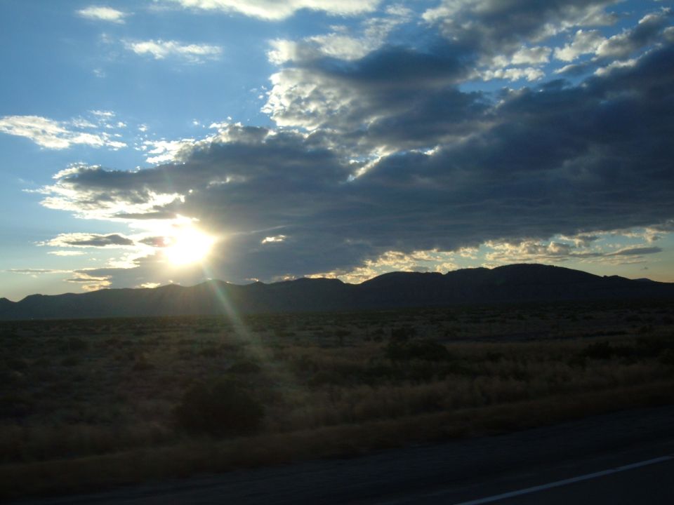 Sun shining through clouds over mountains and a plain.