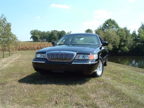 2001 Mercury Grand Marquis - A black 2001 Mercury Grand Marquis is parked on a grassy hill next to a pond. The front of the car is facing the camera, showing its chrome…