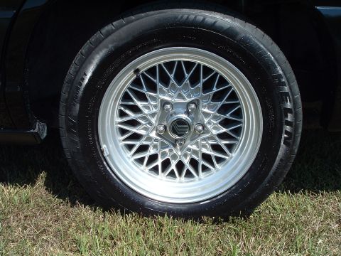 2001 Mercury Grand Marquis - A close-up, low-angle shot shows the front driver's side tire and a silver mesh alloy wheel of a black sedan. The tire is shiny and appears…