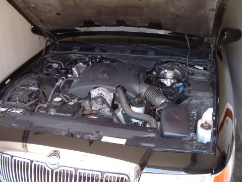 2001 Mercury Grand Marquis - The engine bay of a black 2001 Mercury Grand Marquis is shown with the hood open. The engine, alternator, coolant reservoir, and various ho…