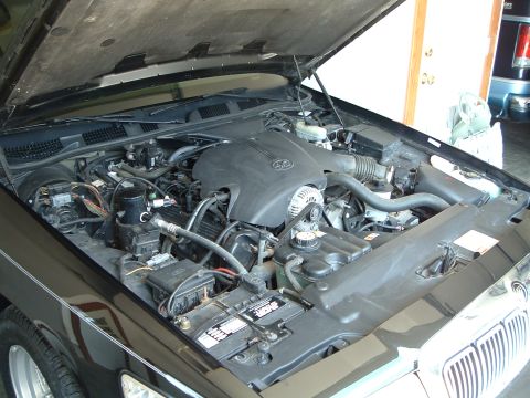 2001 Mercury Grand Marquis - The engine bay of a black 2001 Mercury Grand Marquis is shown with the hood open. The engine, battery, and various hoses and wires are visi…