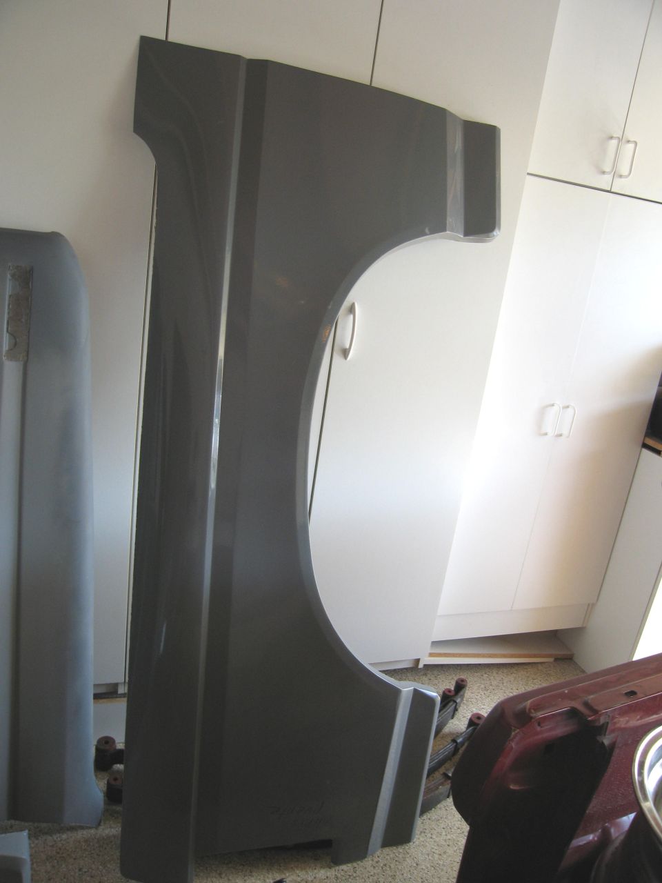 Gray fender and bumper cover next to white cabinets, with a red vehicle part in the foreground.