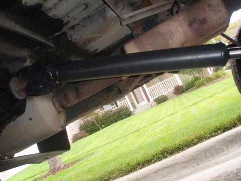 1987 Ford Bronco - The underside of a vehicle shows a black driveshaft connecting to a differential. A portion of the exhaust system is visible above the driv…