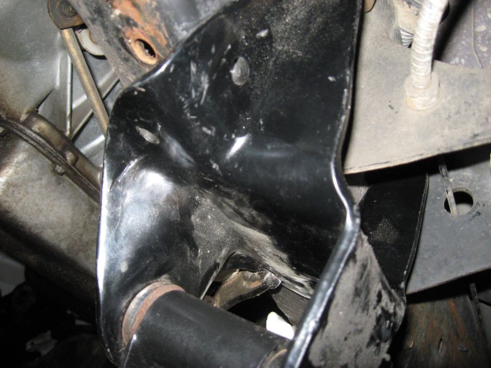 Underside view of a black metal vehicle bracket with rust on surrounding parts.