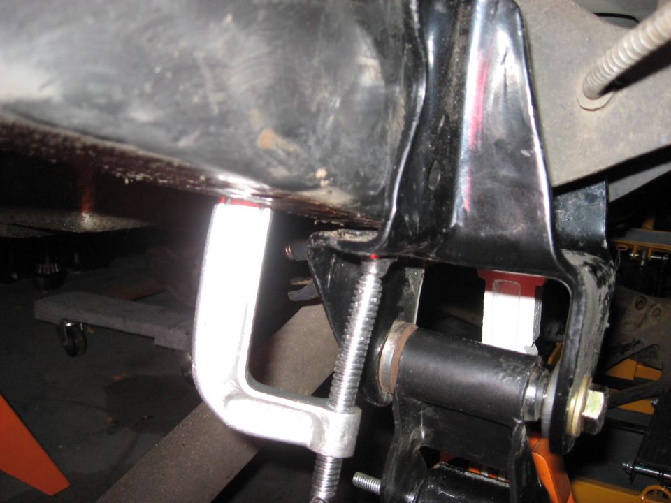 Close-up of a C-clamp holding a black metal bracket on a vehicle underside.