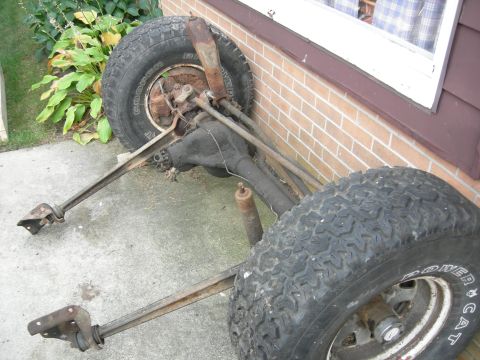 1996 Ford Bronco - A disassembled Ford Bronco rear axle assembly with two large tires and suspension components rests on a concrete surface next to a brick wa…