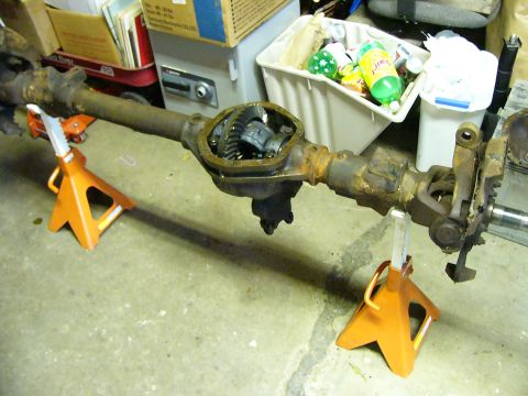 1996 Ford Bronco - A rusty Ford Bronco rear axle assembly is supported by two orange jack stands on a concrete floor. The differential housing is open, reveal…