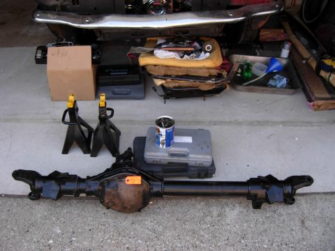 1996 Ford Bronco - A black rear axle assembly is laid out on a concrete surface in front of a vehicle's undercarriage. Various automotive tools and parts, inc…