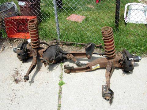 1996 Ford Bronco - A rusty rear axle assembly with coil springs and brake components is laid out on a concrete surface. The assembly appears to be from a 1996…