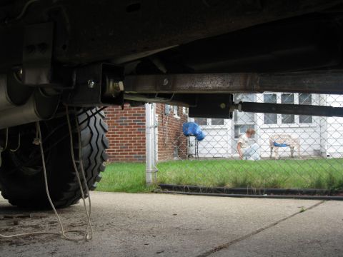 1996 Ford Bronco - Undercarriage view of a modified vehicle, showing a large off-road tire, exhaust system, and suspension components. A person and a dog are…