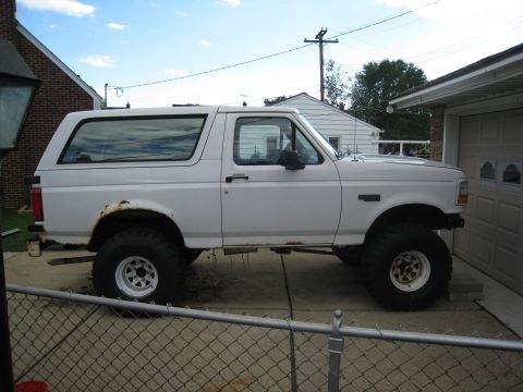 1996 Ford Bronco - A lifted white 1996 Ford Bronco is parked on a concrete driveway next to a garage. The vehicle has large off-road tires and visible rust ar…