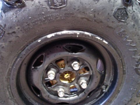 2000 Ford E350 - A close-up, wet tire and rim of a 2000 Ford E350. The tire has visible text and tread, and the black rim has five lug nuts.