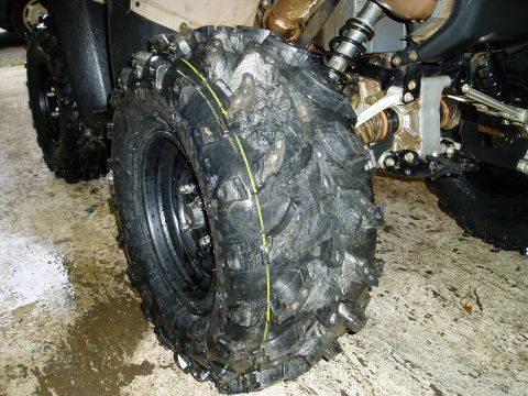2000 Ford E350 - A close-up view of a large, knobby off-road tire on a vehicle, likely an ATV, with a wet, muddy tread and a yellow stripe on the sidewall.…
