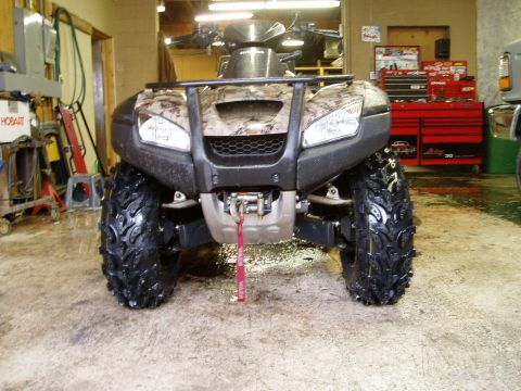 2000 Ford E350 - A front view of a camouflage-patterned ATV parked on a wet concrete floor in a garage. The ATV has large, knobby tires and a red tow strap…