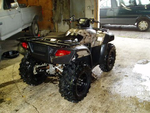 2000 Ford E350 - A camouflage-patterned ATV is parked on a wet concrete floor next to a light-colored pickup truck. The ATV has large, knobby tires and a re…