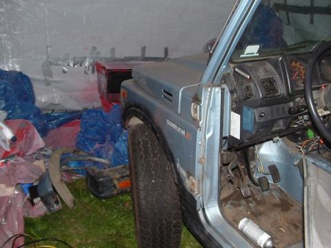 2001 Ford F-350 - The interior of a Suzuki Samurai shows its dashboard and pedals, surrounded by various items in a storage area.