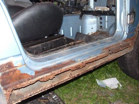 2001 Ford F-350 - The door sill of a light blue vehicle exhibits severe rust, indicating significant deterioration and damage.