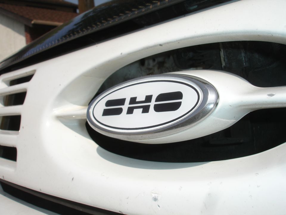 Close-up of a white oval SHO emblem on a car grille