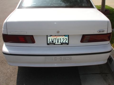 1990 Ford Taurus - The rear of a white Ford Taurus features 'TAURUS' badging and a prominent 'SHO' emblem.