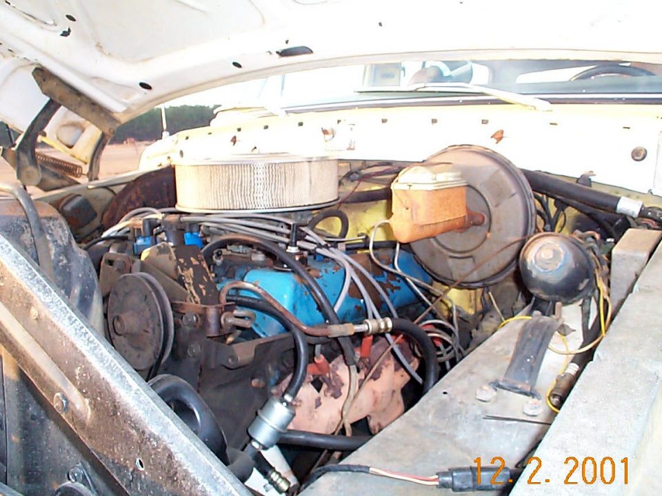 Engine bay with blue V8 engine, round air cleaner, and rusty components; dated 12.2.2001