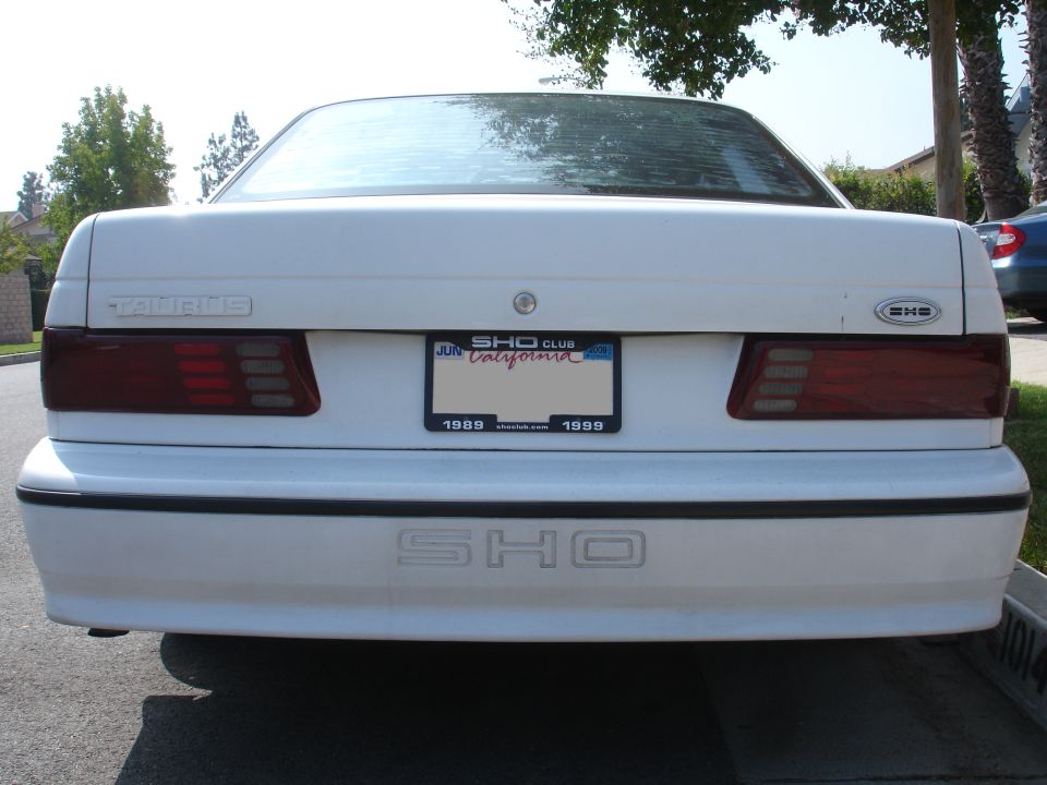 White Ford Taurus SHO rear with California license plate frame showing 1989 and 1999