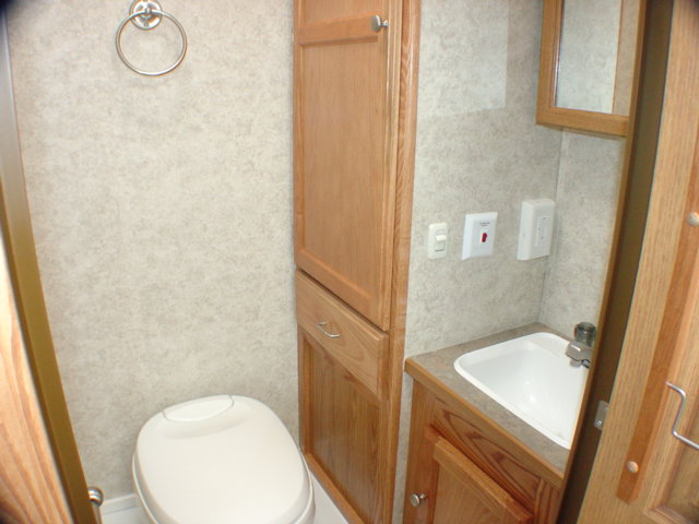 RV bathroom interior with white toilet, oak cabinets, small oval sink and towel ring