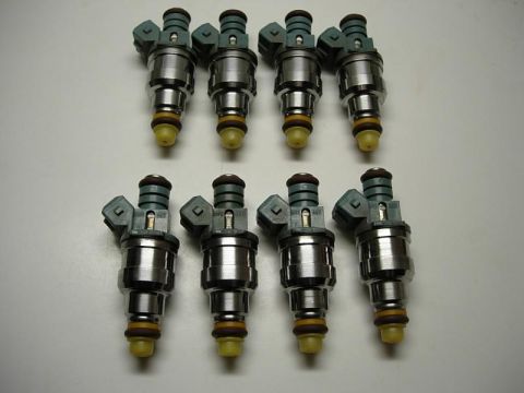 1993 Ford Bronco - Eight fuel injectors are laid out on a white surface, with a Supermotors.net watermark in the lower right corner.