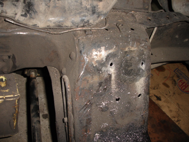 Rusty frame crossmember under a vehicle with drilled holes and scraped undercoating during repair
