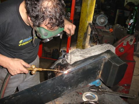 1980 Ford Bronco - A mechanic uses a welding torch on a metal component in a garage setting.