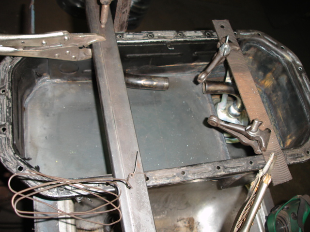 Oil pan being worked on with vise grips, clamps, and metal bar