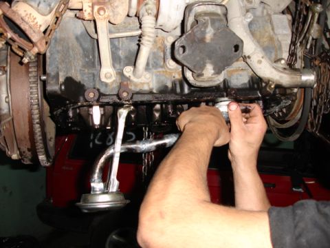 1980 Ford Bronco - Mechanic's hands are shown removing the oil pan from a vehicle engine.