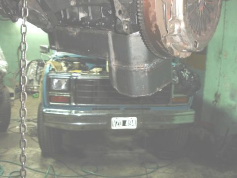 1980 Ford Bronco - A blue 1980 Ford Bronco's front end is visible as its engine is worked on, suspended by chains.