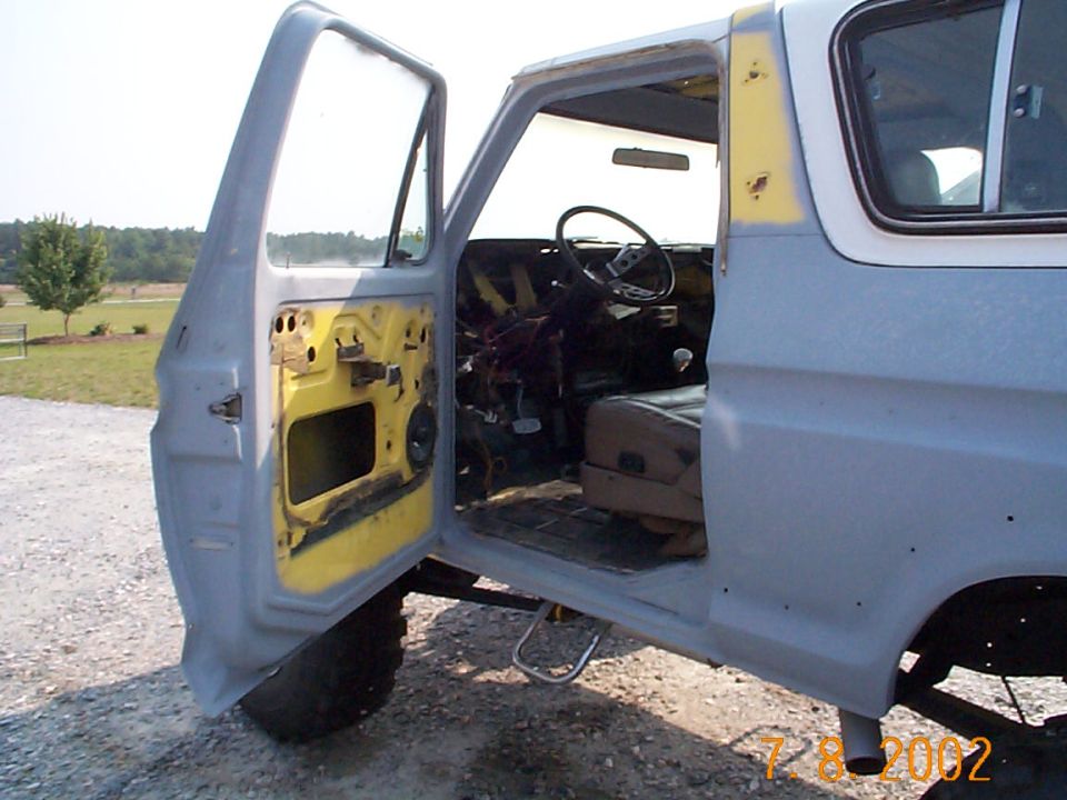 Primer-gray truck cab with door open showing stripped yellow interior and bare door panel