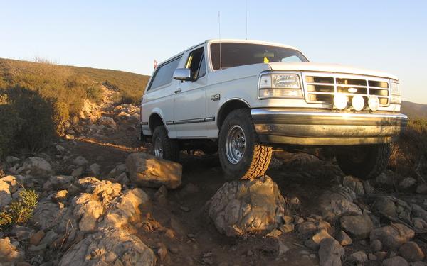 White lifted Ford Bronco with off-road tires and bumper lights climbing over boulders on a rocky trail