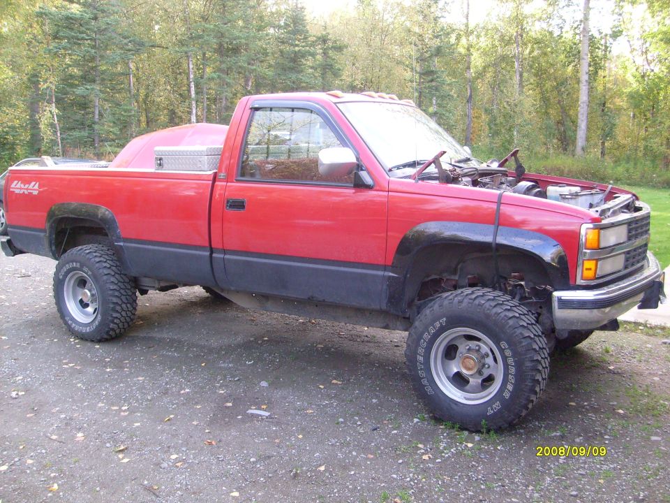 Red pickup truck, hood open, showing engine bay. Appears to be a 1990s Chevrolet/GMC