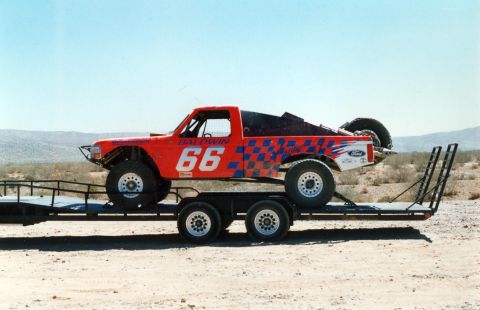 1984 Ford Bronco - A custom-built off-road truck, likely a modified Ford, is transported on a flatbed trailer under a clear blue sky.